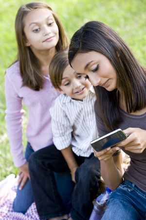 Teenage girl texting on mobile phone while younger siblings watchの写真素材
