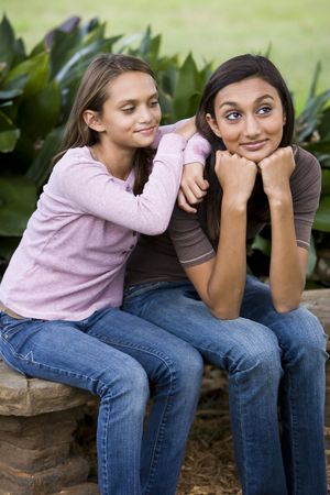 Teenage girl with younger sister sitting together on bench outdoorsの写真素材