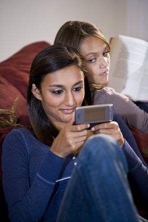 Close-up of teenage girl texting on mobile phone while sister watches from behindの写真素材