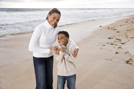 Happy African-American mother and ten year old son standing together on beach