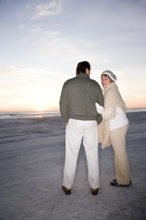 Affectionate senior couple in sweaters on beach at dawnの写真素材