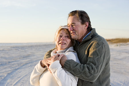Affectionate senior couple in sweaters together on beach 