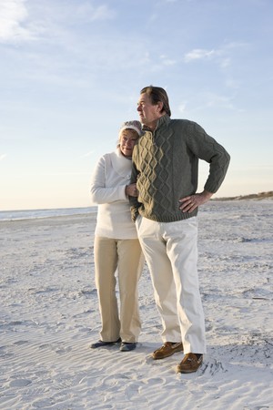 Affectionate senior couple in warm clothing standing together on beachの写真素材