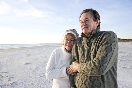 Affectionate senior couple in warm clothing standing together on beachの写真素材