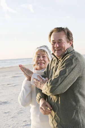 Affectionate senior couple in warm clothing standing together on beachの写真素材