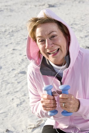 Senior woman exercising,  lifting hand weights on beachの写真素材