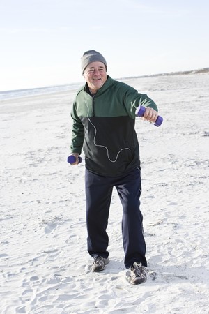 Senior man exercising with hand weights on beach listening to musicの写真素材