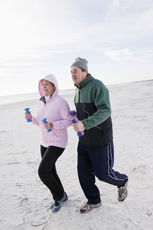 Senior couple exercising, jogging on beach with hand weightsの写真素材