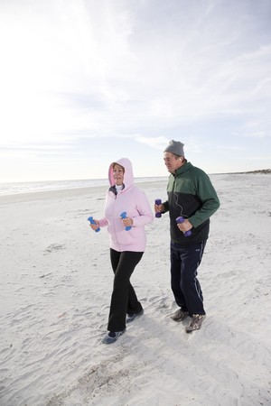 Senior couple exercising, walking on beach with hand weightsの写真素材