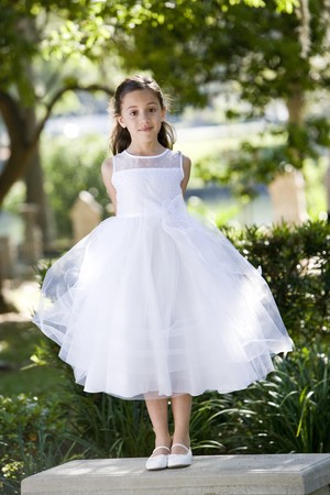 Beautiful child wearing formal white dress standing on park benchの写真素材
