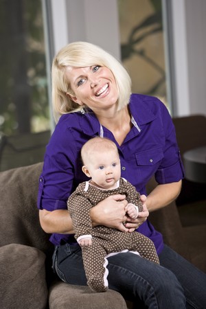 Happy mother holding 3 month old baby on couch at homeの写真素材