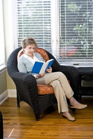 Senior woman sitting on living room chair reading bookの写真素材