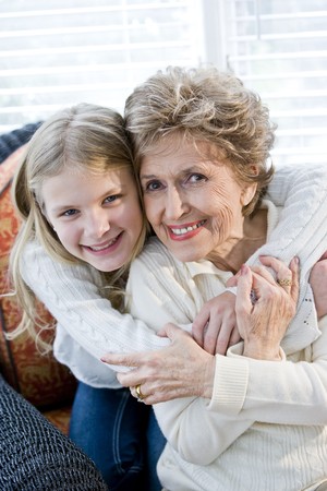 Portrait of happy young girl hugging grandmother at homeの写真素材
