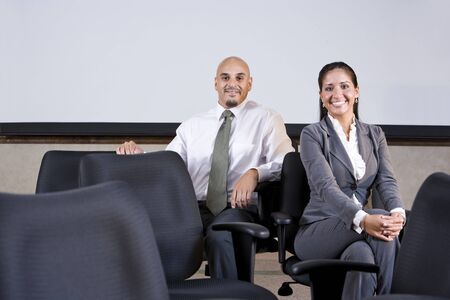 Professional Hispanic office workers sitting on chairs in boardroom by whiteboardの写真素材