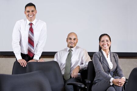 Professional Hispanic office workers sitting on chairs in boardroom by whiteboardの写真素材