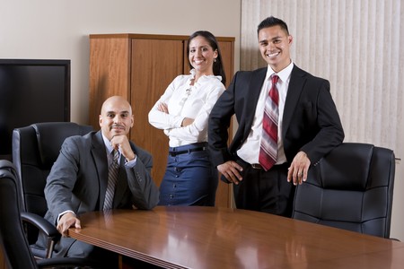 Three Hispanic business people smiling in boardroomの写真素材