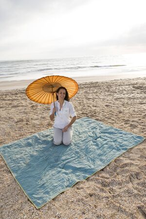 Mid-adult Hispanic woman with parasol on beach blanketの写真素材