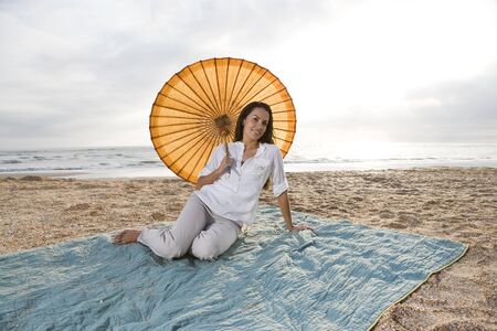 Mid-adult Hispanic woman with parasol on beach blanketの写真素材