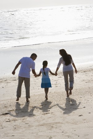 Rear view of Hispanic family with 9 year old girl holding hands walking on beachの写真素材