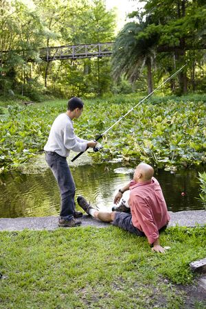 Hispanic 14 year old teen boy and father fishing in pondの写真素材