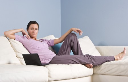 Portrait of mid-adult woman relaxing on couch at home with laptopの写真素材