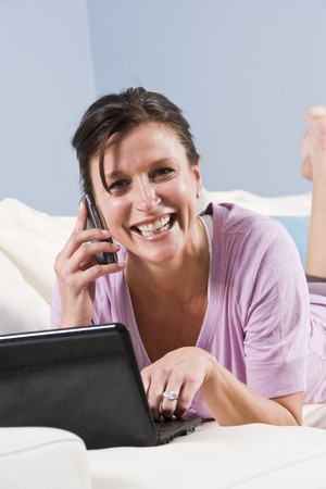 Modern woman relaxed on couch with mobile phone and laptop computerの写真素材