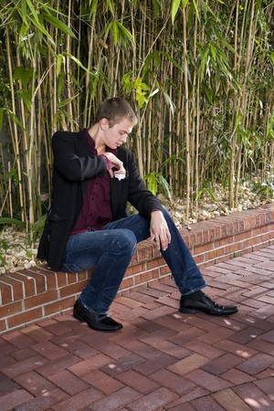 Young well-dressed man sitting on patio fixing handkerchiefの写真素材
