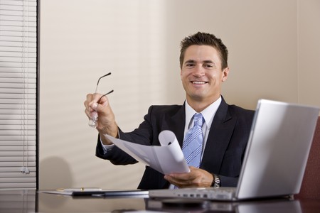 Businessman with laptop working in boardroom reading reportの写真素材