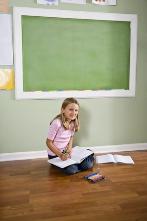Back to school - girl writing in classroom by green blackboard, 8 years oldの写真素材
