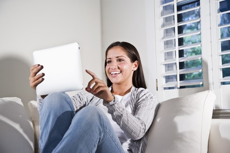 Hispanic woman using tablet computer relaxing on couchの写真素材