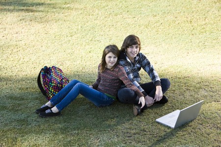 Boy and girl sitting on grass with laptop, online in parkの写真素材
