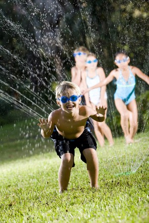Happy boy (7 years) soaked by lawn sprinkler, friends in backgroundの写真素材