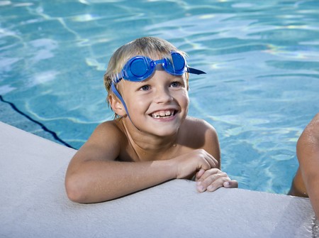 Happy boy with swim goggles looks up at side of swimming pool, 7 yearsの写真素材