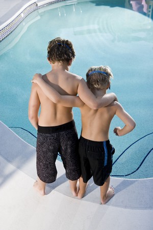 Boys, 7 and 9, looking down at water in swimming poolの写真素材