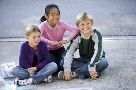 Three kids sitting on driveway smiling.  Ages 7 to 9の写真素材