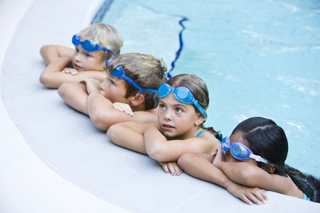 Multi-ethnic kids, resting in a row on side of swimming pool, ages 7 to 9.  Selective focus on Caucasian girlの写真素材