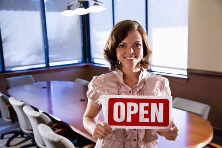 Young office worker holding open sign in empty boardroomの写真素材