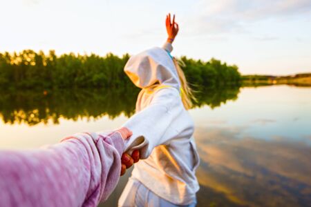 Girl in a white hoodie holding a guy's hand on the beachの写真素材