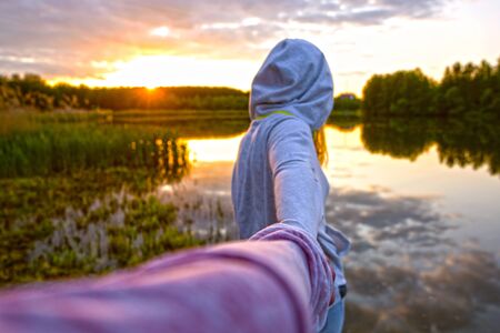 Girl in a white hoodie holding a guy's hand on the beach at the sunsetの写真素材