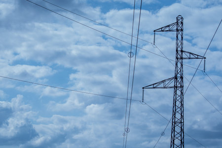 High voltage power lines and pylons against blue sky with clouds