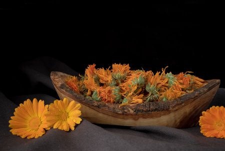 Dried calendula flowers in a wooden bowl on a black backgroundの写真素材