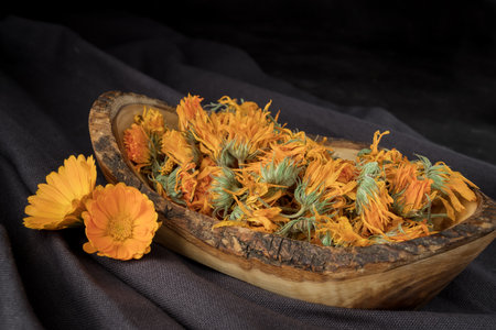 Dried calendula flowers in a wooden bowl on black fabric backgroundの写真素材