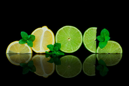 Lime slices and mint leaves on a black background with reflection.の写真素材