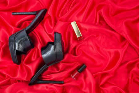 Black high heel shoes and lipstick on red satin background, top viewの写真素材