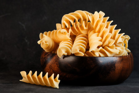 Raw uncooked Italian pasta fusilli in wooden bowl on black backgroundの写真素材
