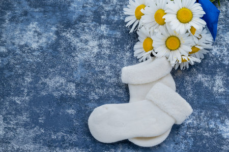Baby booties and chamomile bouquet on blue background