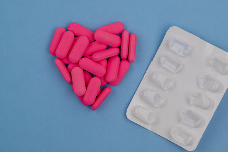 Pink pills in the shape of a heart on a blue background.の写真素材