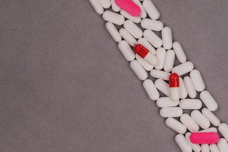 Top view of white and pink pills on grey background with copy space