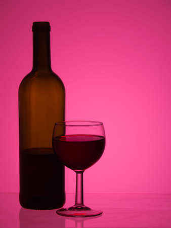 Wine bottle and glass over bright pink background with copy space.の写真素材