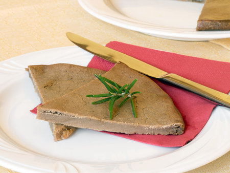 Castagnaccio slice on plate with rosemary. Italian local cuisine (Lunigiana)Domestic setting.の写真素材
